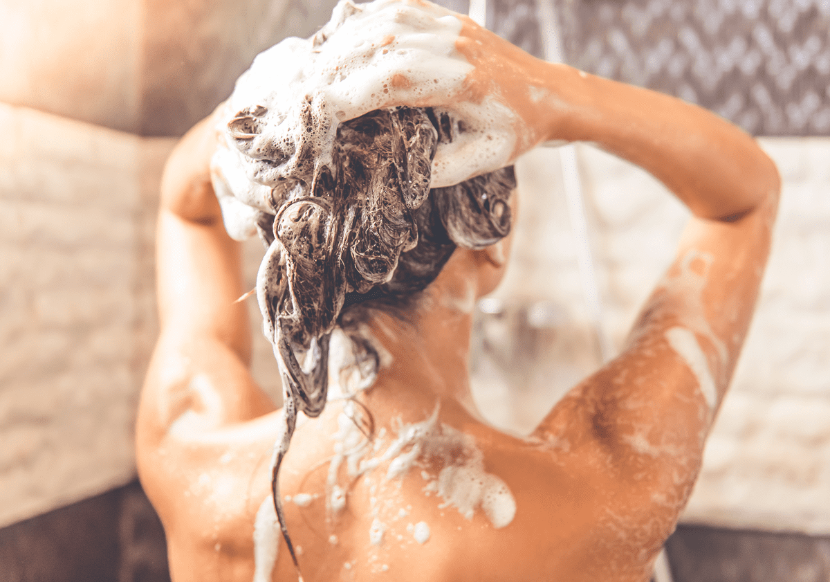 Frau unter der Dusche seift sich die Haare ein
